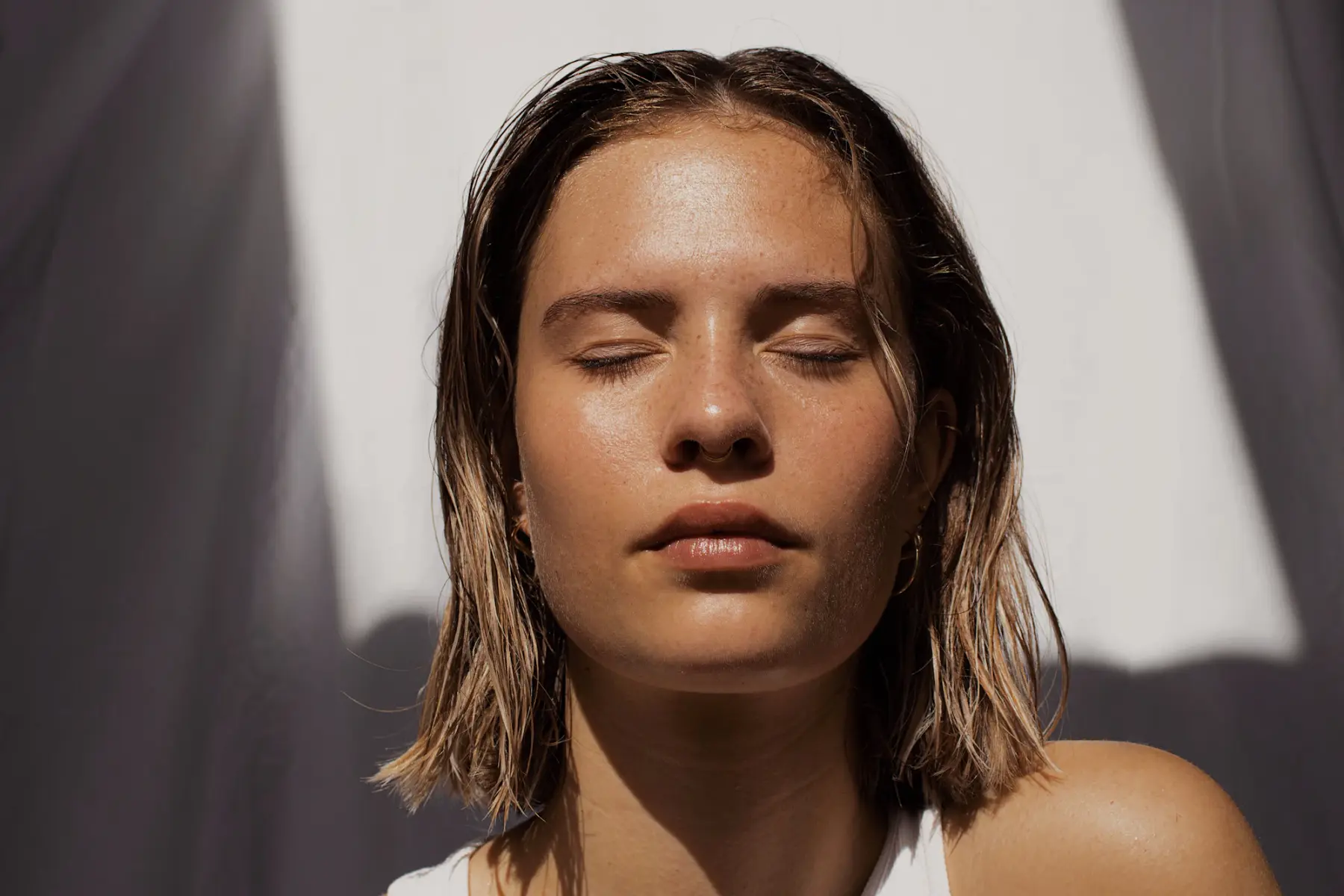 Mulher de cabelo molhado e olhos fechados, com o rosto banhado por luz quente do sol
