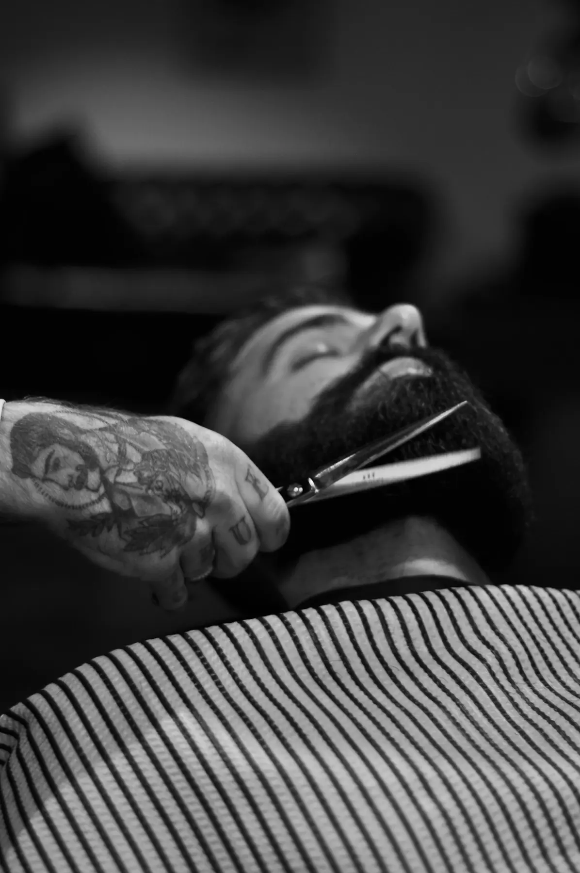 Mão tatuada aparando uma barba com tesoura, em preto e branco