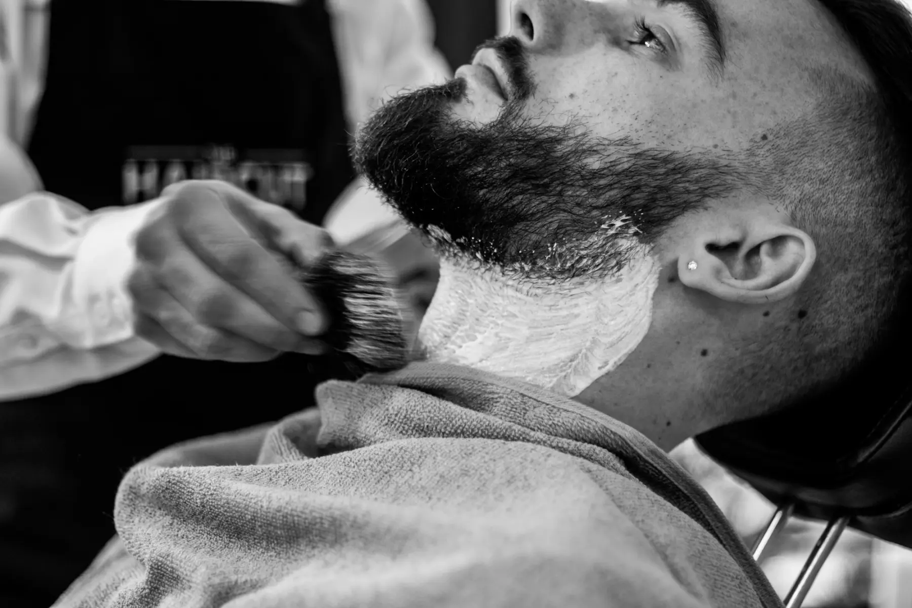 Pincel aplicando espuma de barbear no rosto de um cliente, em preto e branco