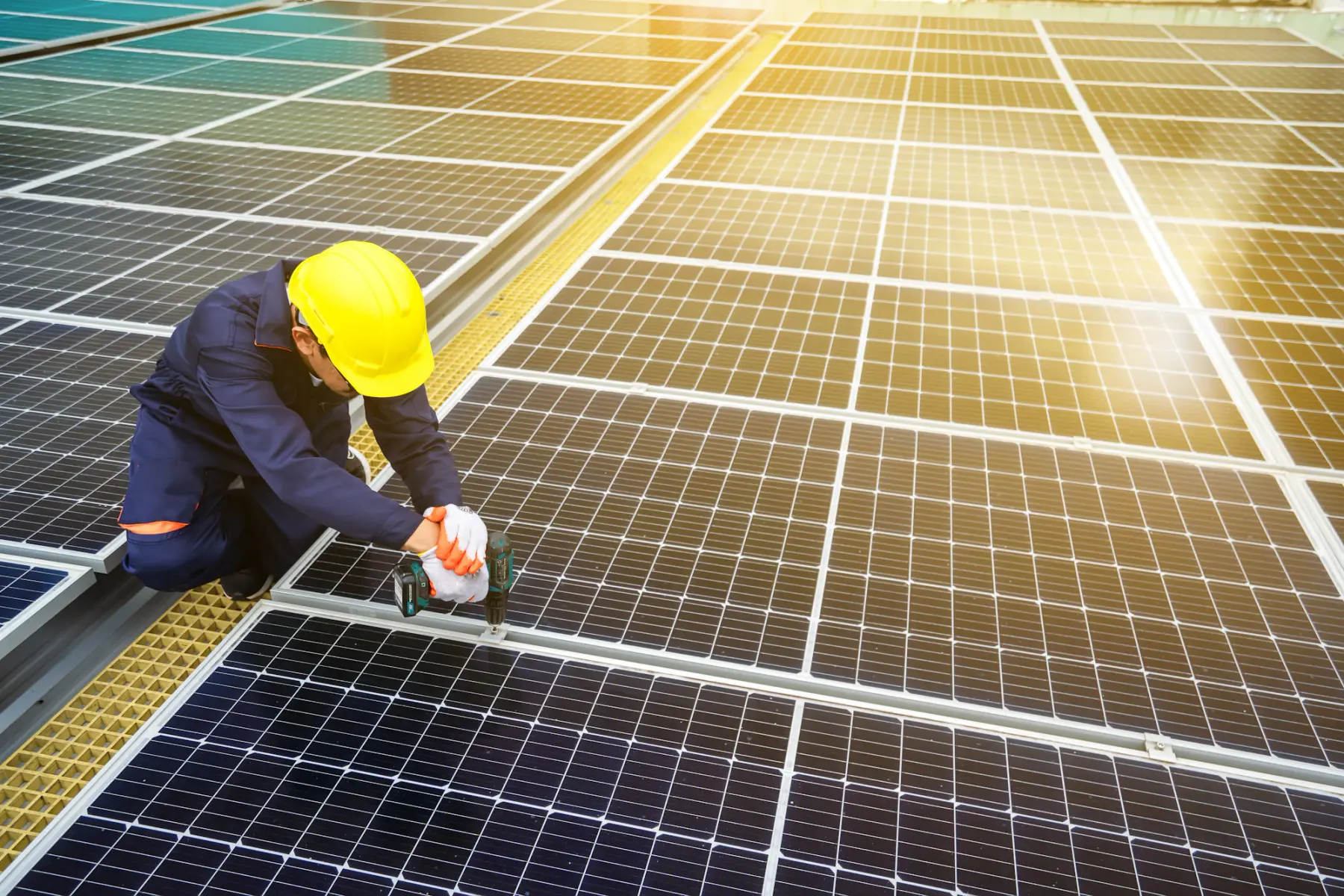 Instalador de capacete amarelo e luvas fixa a estrutura de uma placa solar com parafusadeira