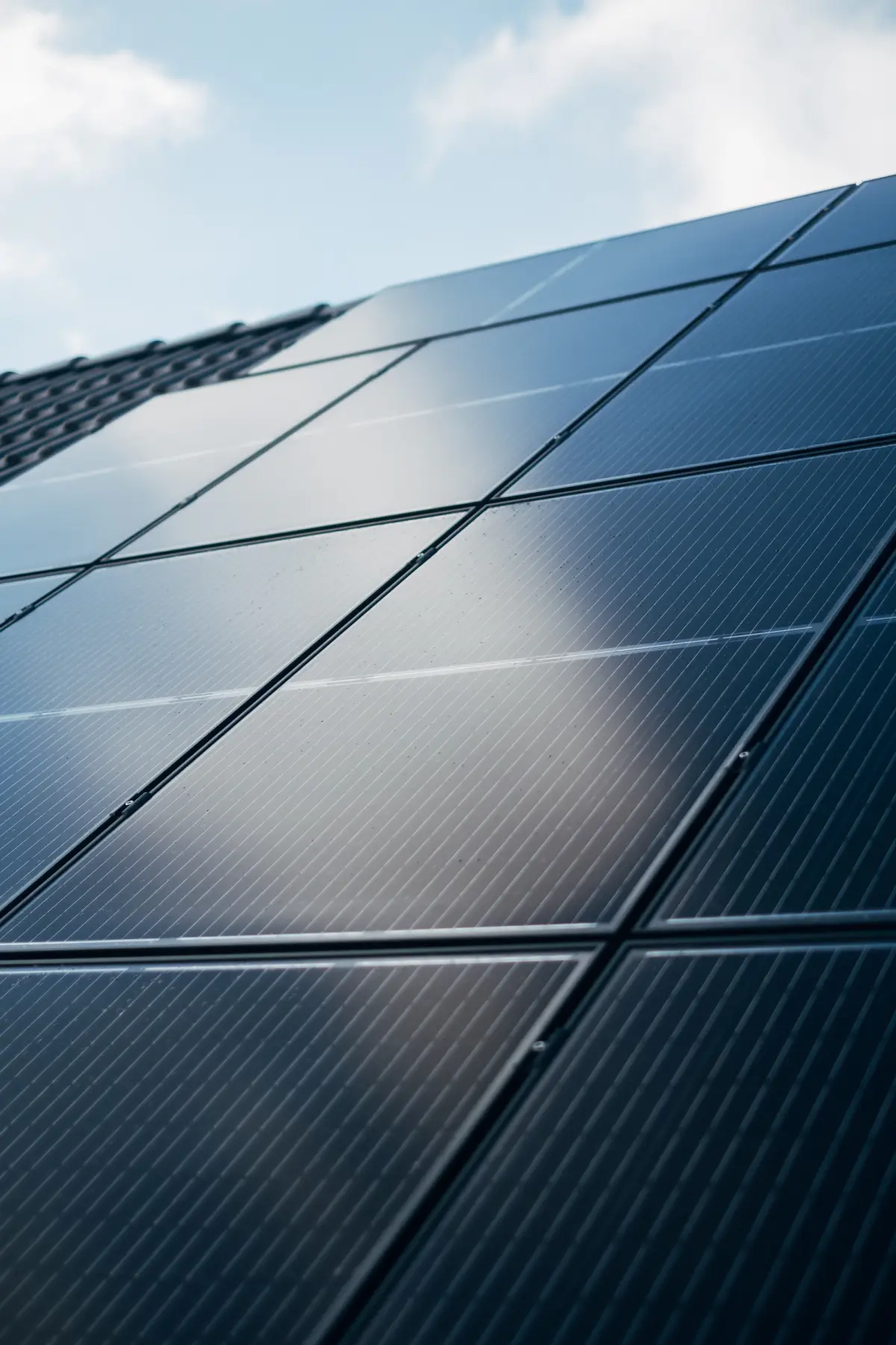 Placas solares escuras num telhado, refletindo o céu claro