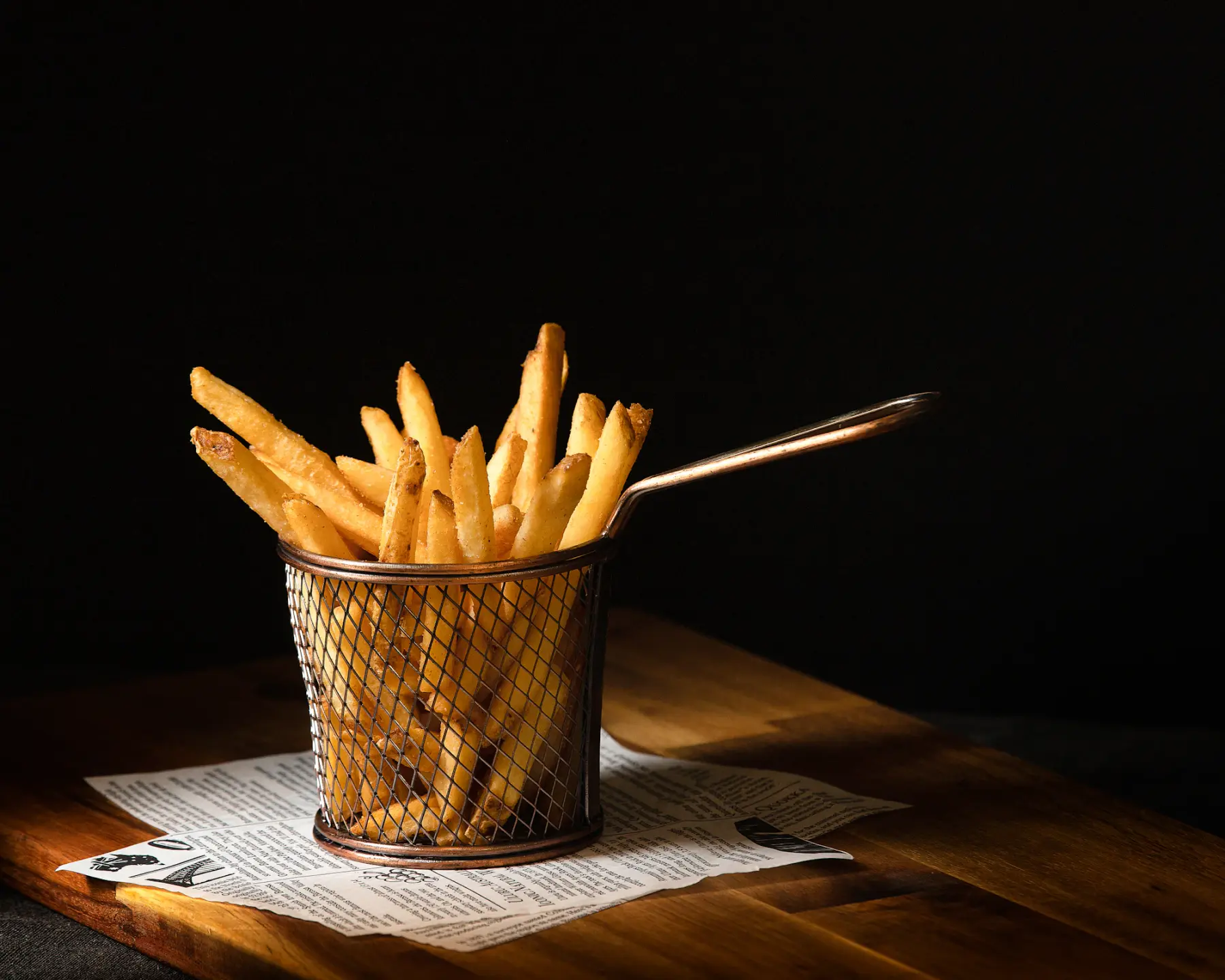 Batatas fritas em cestinha de metal sobre papel