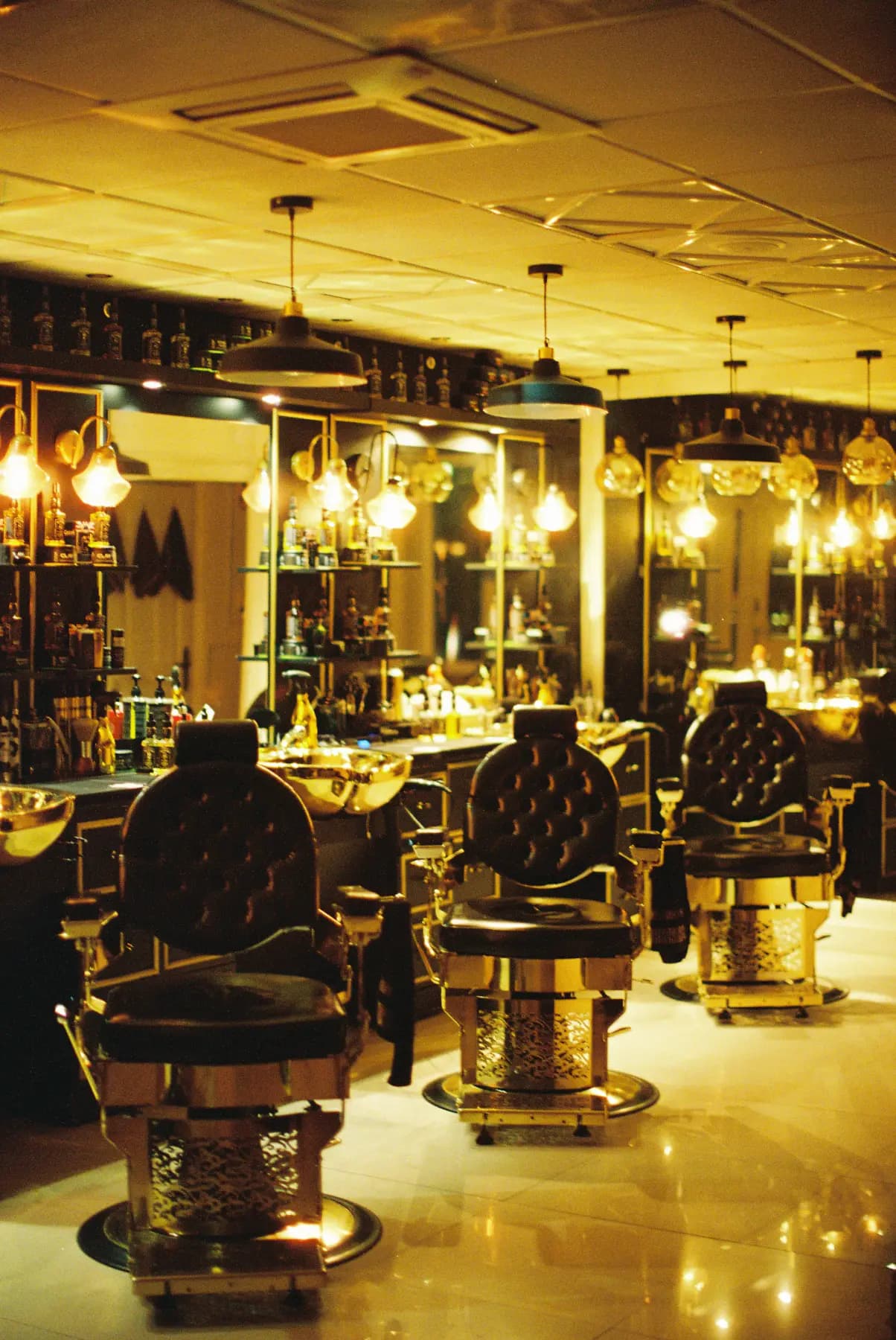 Salão de barbearia com cadeiras de couro e luminárias douradas