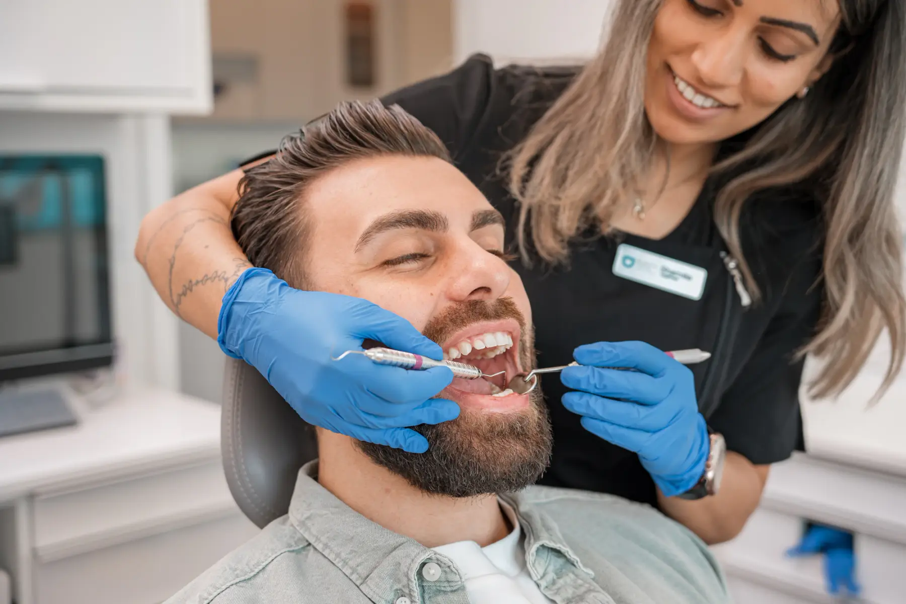 Dentista de luvas examina os dentes de um paciente sorridente na cadeira