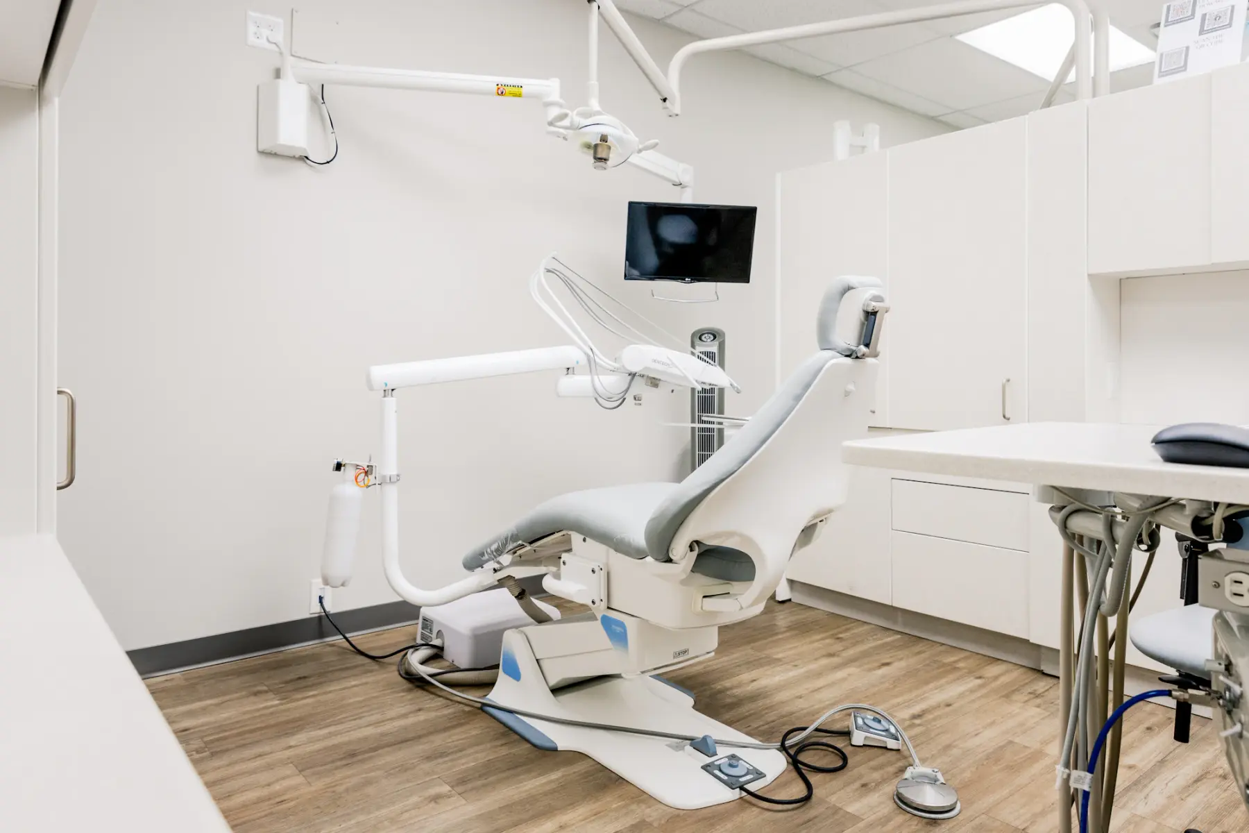 Sala de atendimento clara, com cadeira odontológica, monitor e armários brancos