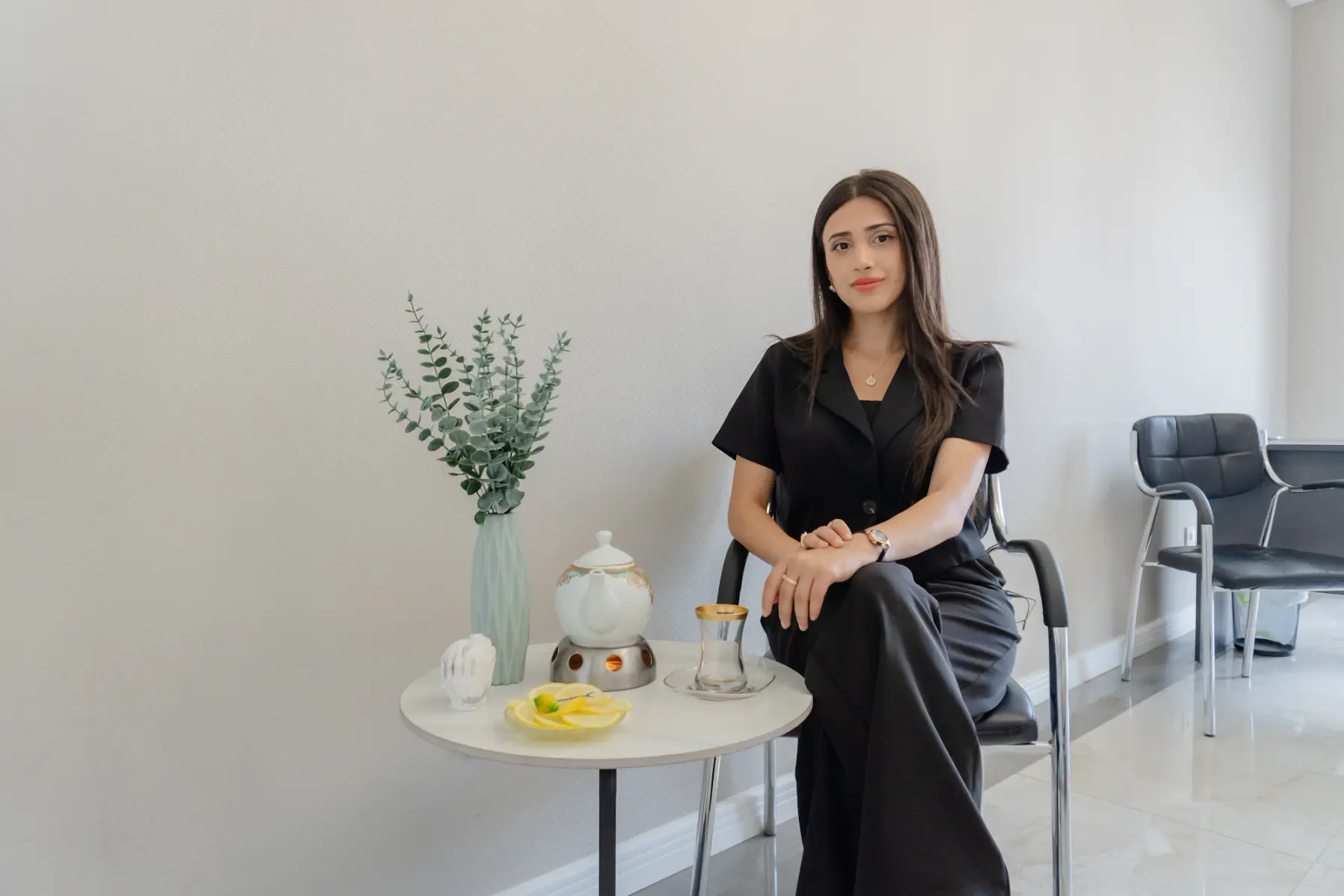 Mulher sentada na recepção, ao lado de uma mesa com chá e um vaso de eucalipto