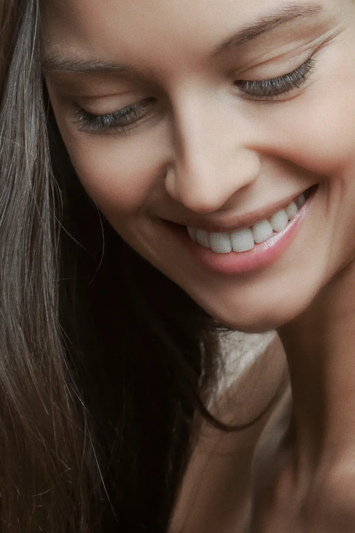 Close de uma mulher sorrindo de olhos baixos, com os dentes superiores à mostra