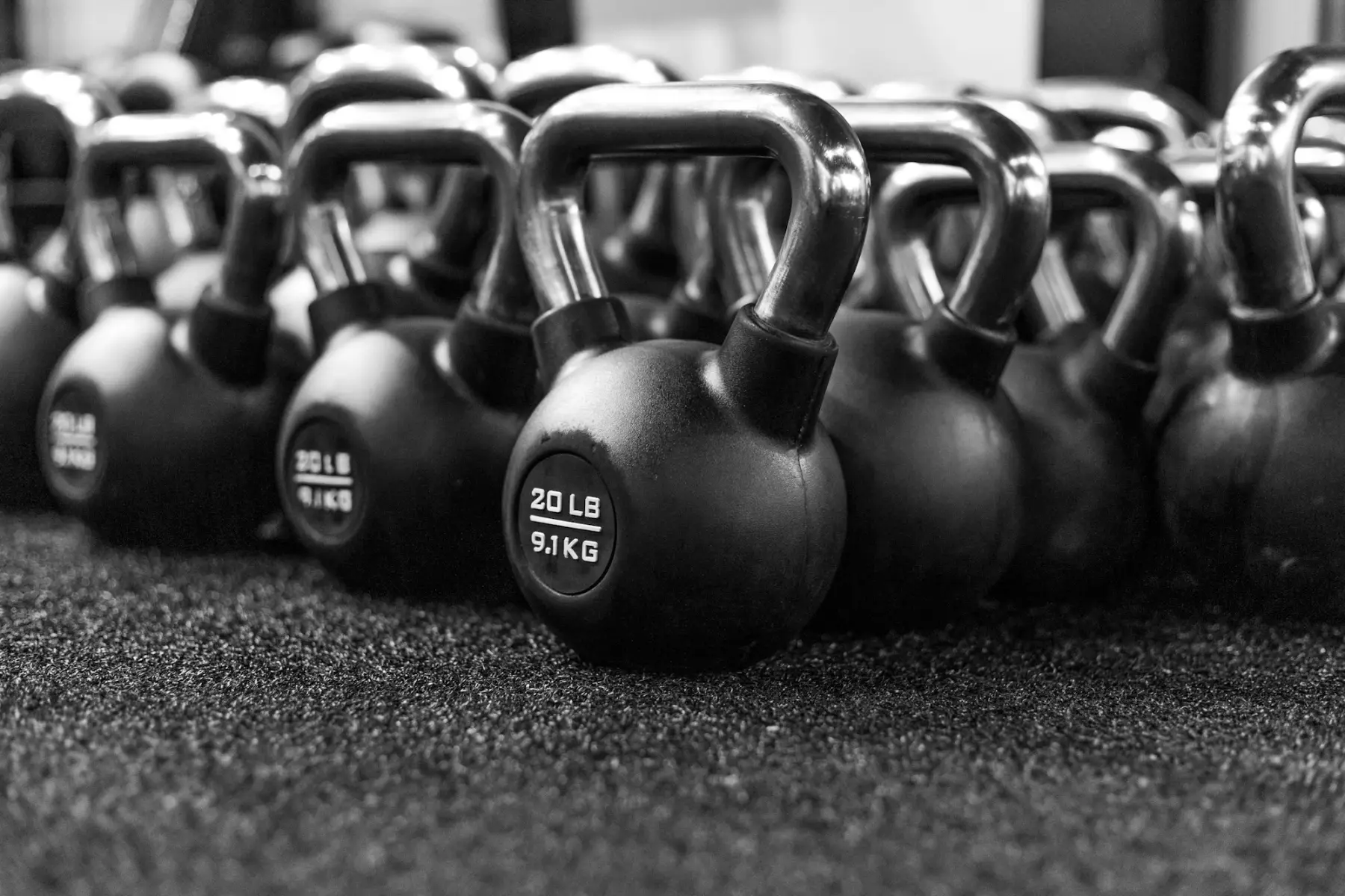 Fileira de kettlebells pretos de diferentes pesos sobre o piso emborrachado