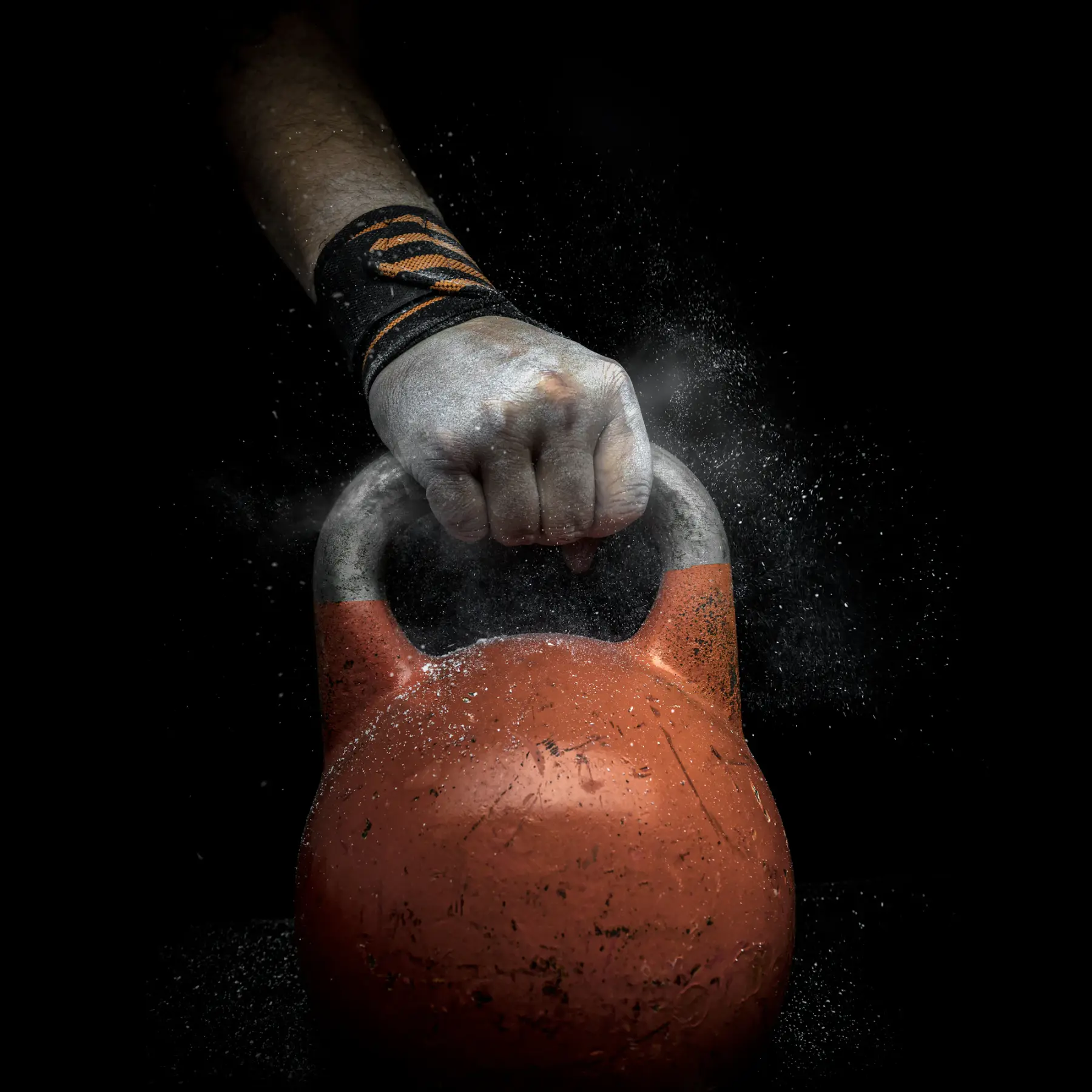 Mão coberta de magnésio segurando a alça de um kettlebell sobre fundo preto