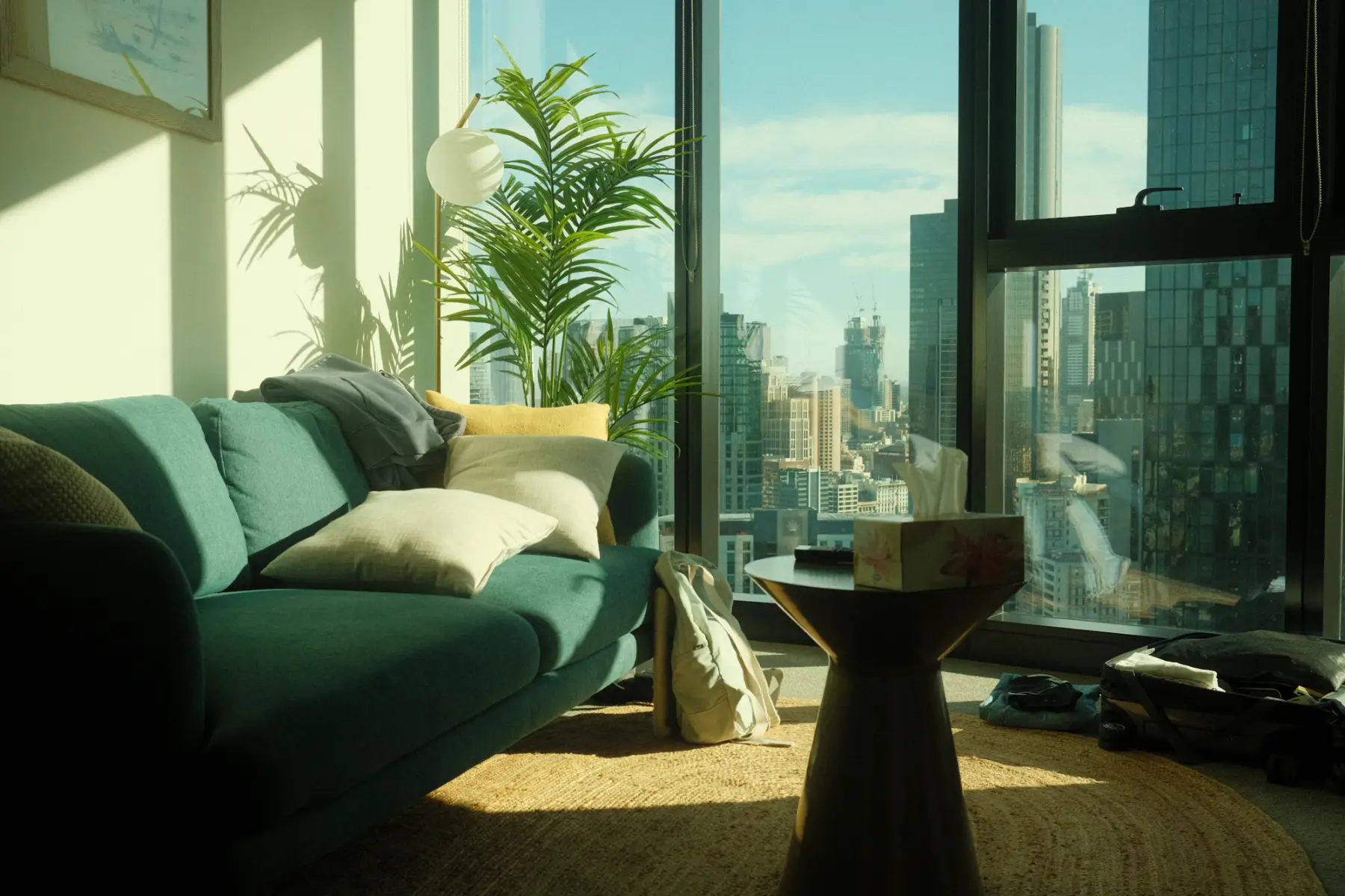 Sala de apartamento com sofá verde e janelas do piso ao teto com vista para prédios da cidade